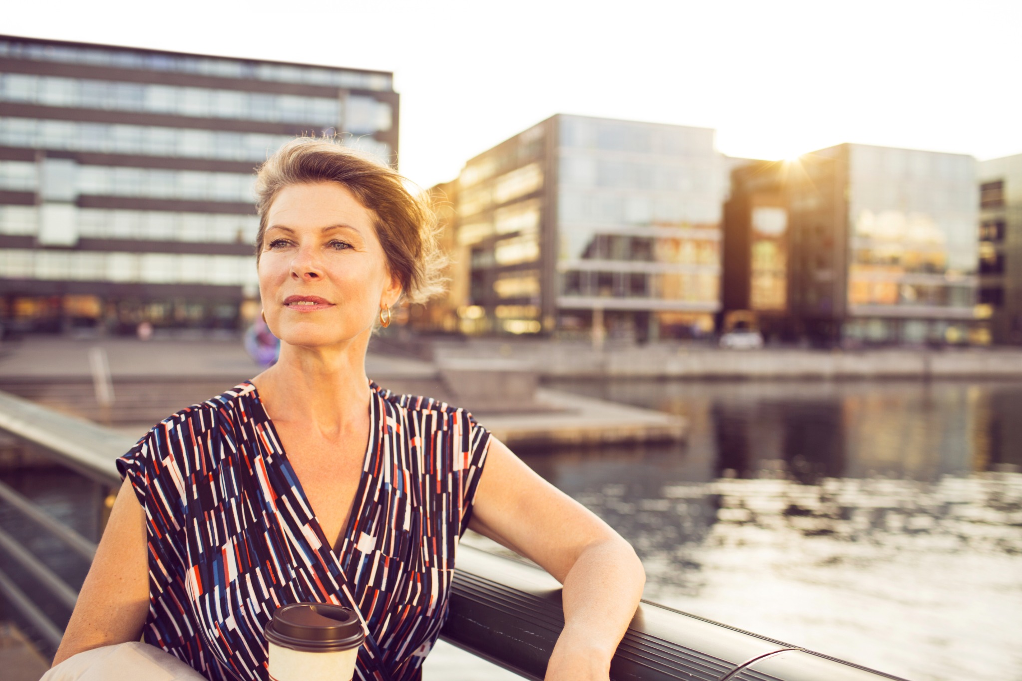 A woman holding a cup, relaxing on a city bench