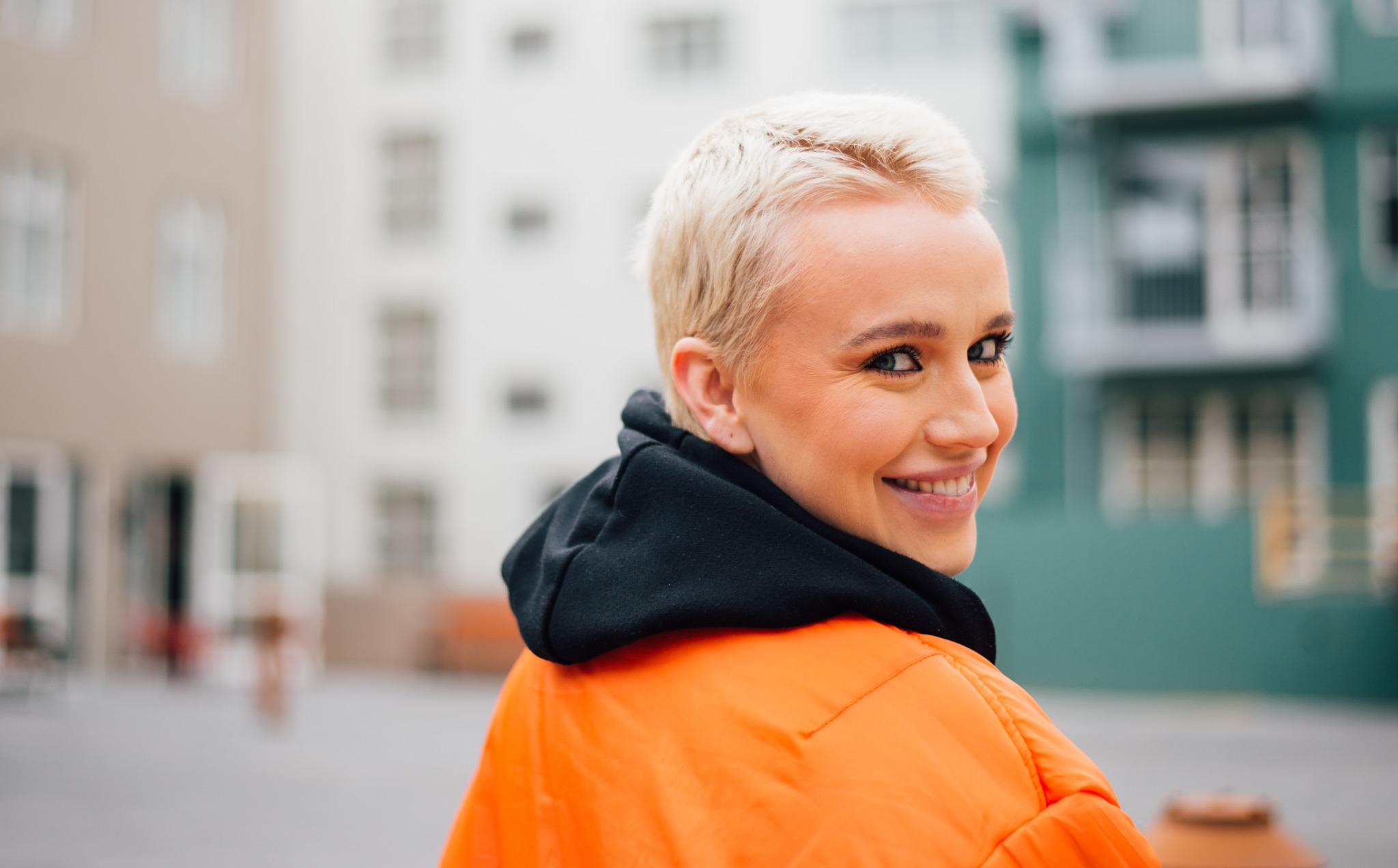 A woman with short blonde hair and an orange jacket